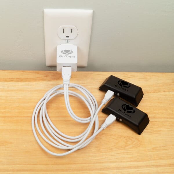 Bi-Tapp charger plugged into wall with cable to charge two tappers at a time.